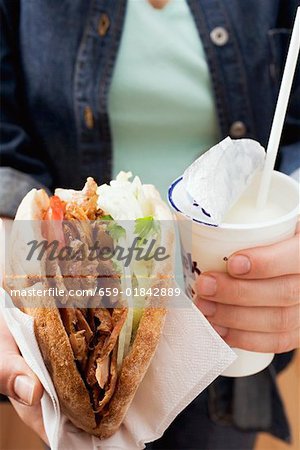 Hands holding a döner kebab and drinking yoghurt