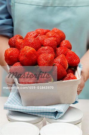 Woman holding punnet of strawberries, jam jars