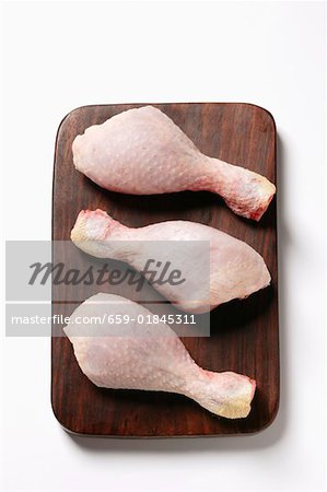 Three raw chicken legs on chopping board
