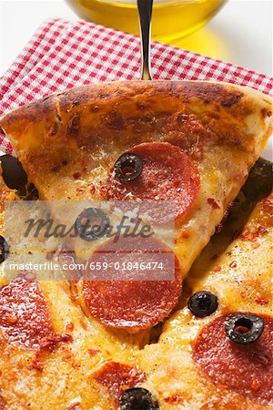 Pizza with salami, cheese and olives, a piece cut