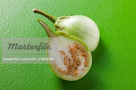 Green baby aubergine, halved, on green background