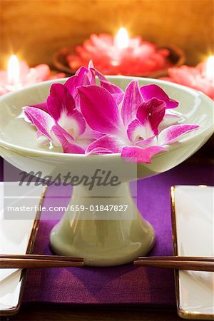 Thai table decoration: orchids in bowl of water, candles