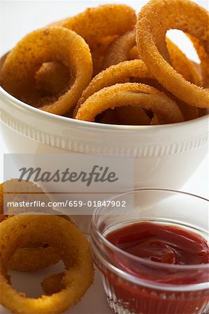 Deep-fried onion rings in white bowl, ketchup
