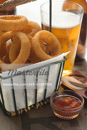 Deep-fried onion rings in wire basket, ketchup, beer, salt