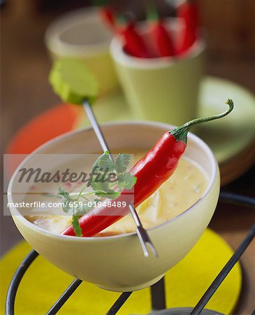 Chili pepper on fondue stick above cheese and chili sauce