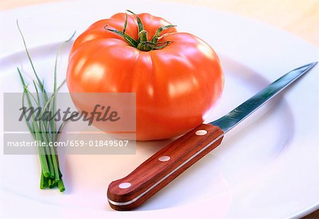 A tomato, chives and a knife on a plate