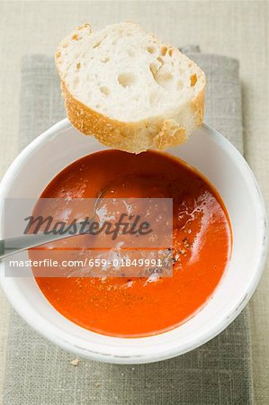 Creamed pepper soup in soup bowl, spoon & slice of baguette