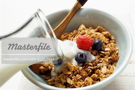 Pouring milk over crunchy muesli with berries in bowl