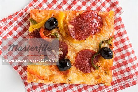 A slice of salami pizza with peppers and olives