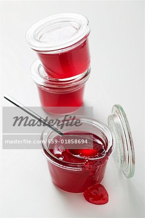 Three jars of redcurrant jelly, one opened, with spoon