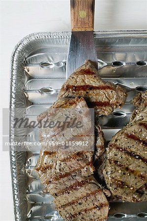 Grilled meat in aluminium grill tray (overhead view)