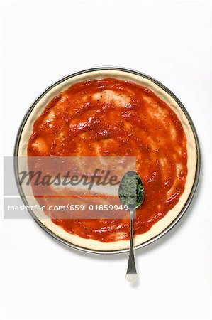 Pizza base with tomato sauce and spoonful of oregano