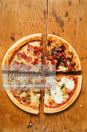 Pieces of four different pizzas on wooden background