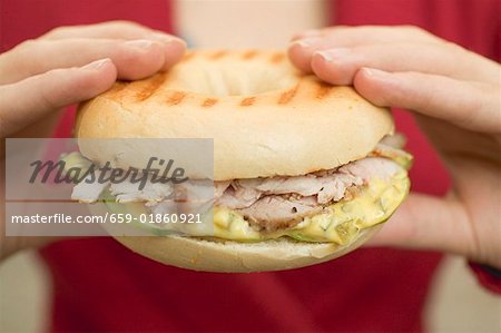 Hands holding bagel with pork fillet & honey mustard relish Hands holding bagel with pork fillet & honey mustard relish