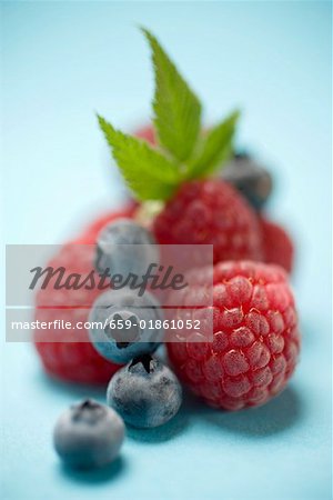 Blueberries and raspberries with leaves on blue background Blueberries and raspberries with leaves on blue background