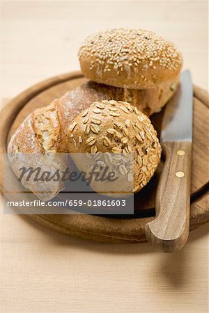 Baguette and wholemeal rolls on breadboard with knife