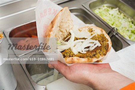 Hand holding opened döner kebab with onions