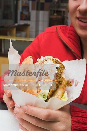 Person holding pita bread filled with falafel in snack bar