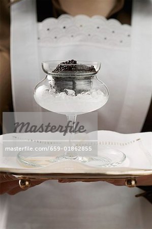 Chambermaid serving caviar in stemmed glass on tray
