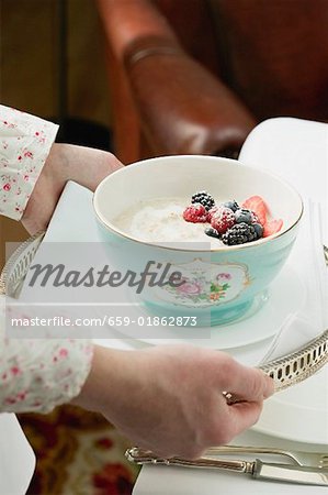 Hands serving bowl of porridge on a tray