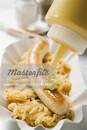 Putting mustard on sausage with sauerkraut Putting mustard on sausage with sauerkraut