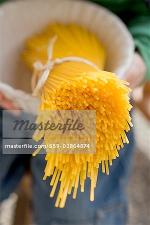 Person holding bowl containing a bundle of spaghetti