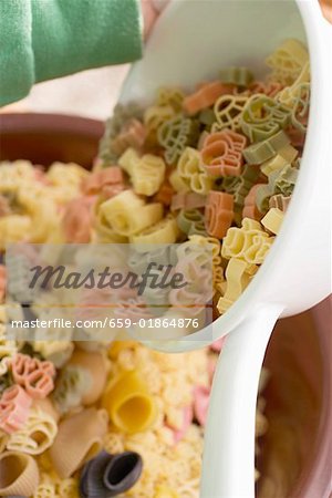 Child tipping coloured pasta out of strainer into bowl