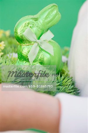 Child's hands holding green Easter Bunny on grass