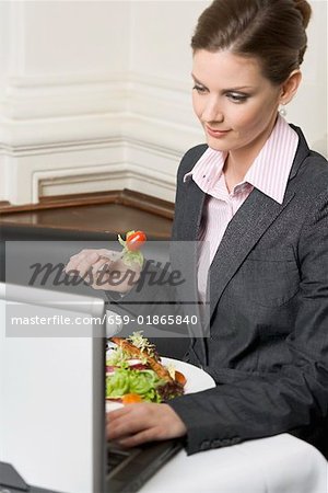Woman with laptop eating salad in restaurant