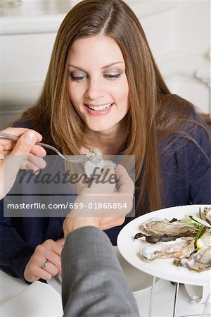 Man offering woman fresh oyster in restaurant