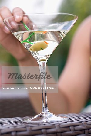 Hand holding green olive on cocktail stick in Martini glass