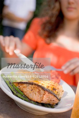 Woman eating grilled salmon with corn on the cob & vegetables