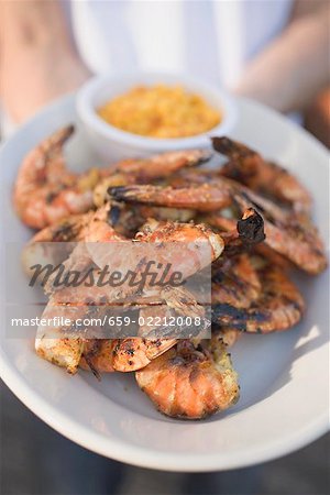 Person holding plate of grilled shrimps