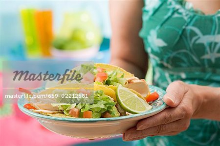 Woman holding plate with two chicken tacos