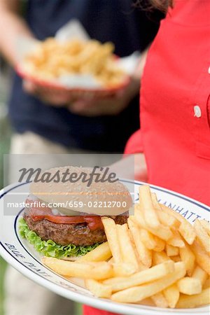 Woman holding plate of hamburger and chips