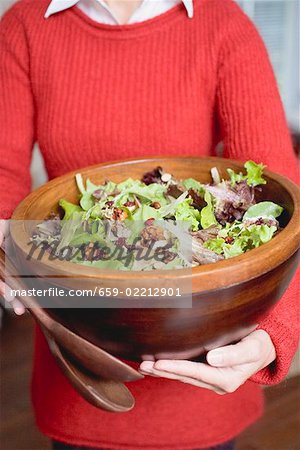 Woman holding large bowl of salad leaves with nuts