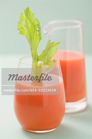 Glass of carrot juice with celery jug in background