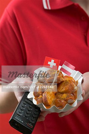 Footballer holding currywurst (sausage with curry sauce) & remote