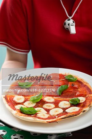 Female footballer holding tomato & mozzarella pizza with basil