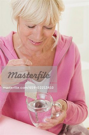 Woman putting tea bag into cup of hot water