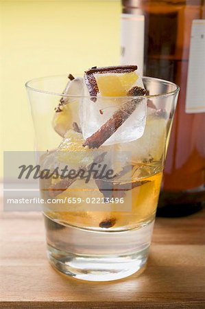 Rum and ice cubes with spices and pieces of fruit in glass