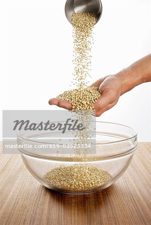 Someone pouring buckwheat over their hand into a glass bowl