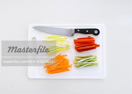 Julienne vegetables on a chopping board with a knife