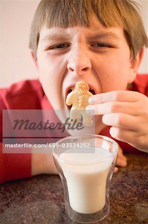 Boy trying to put a whole biscuit in his mouth, glass of milk