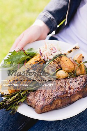 Woman holding plate of steak, grilled vegetables & corn on the cob