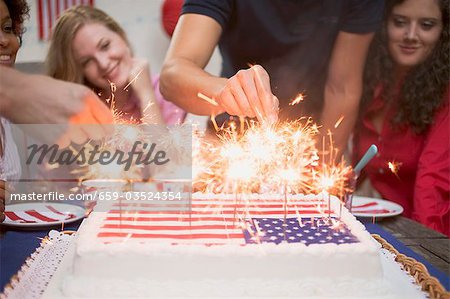 Hands lighting sparklers on a cake (4th of July, USA)