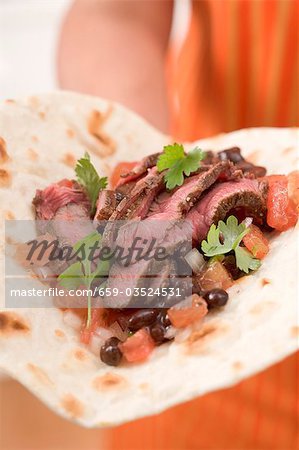 Woman holding beef fajita with beans and tomatoes