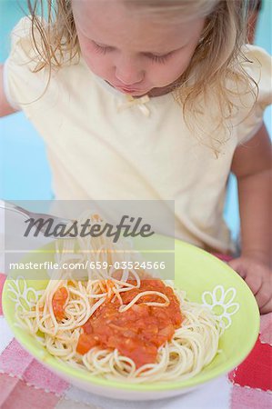 Small girl eating spaghetti with tomato sauce