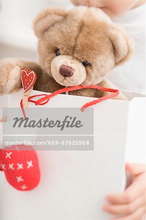 Child holding teddy bear in paper carrier bag