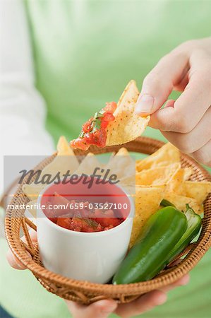 Woman holding basket of nachos with salsa and chilli